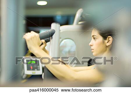 Stock Photography - Woman using weight machine, side view. Fotosearch