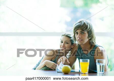 Stock Image - Couple in exercise clothes sitting at table with juice and fruit. Fotosearch