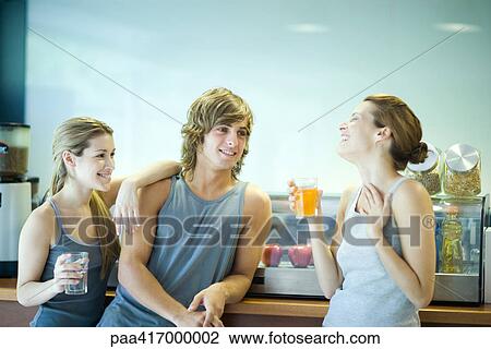 Stock Image - Young adults in exercise clothing taking break in health club cafeteria. Fotosearch