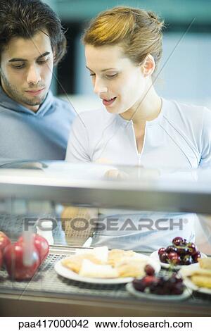 Stock Image - Young adults in exercise clothing having snack in health club cafeteria. Fotosearch