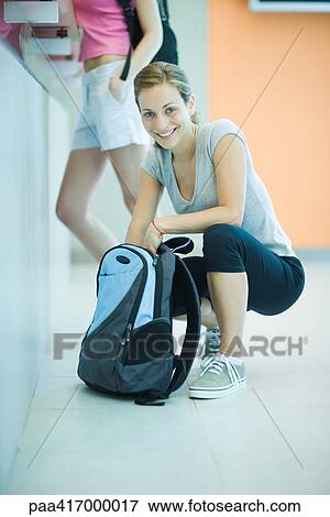 Young woman by counter at health club, squatting down, looking through backpack View Large Photo Image Stock Photo - Young woman by counter at health club, squatting down, looking through backpack. Fotosearch