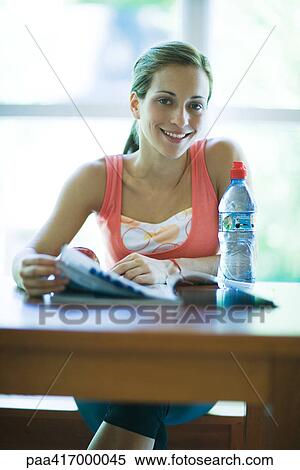 Young woman in exercise clothing, sitting with magazine and bottle of water, smiling at camera View Large Photo Image Stock Photography - Young woman in exercise clothing, sitting with magazine and bottle of water, smiling at camera. Fotosearch