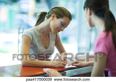 Stock Photo - Young woman signing in at counter of health club. Fotosearch