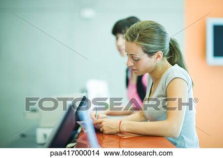 Picture - Young women signing in at counter of health club. Fotosearch