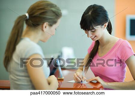 Stock Image - Young women signing in at counter of health club. Fotosearch