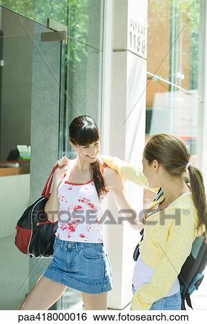 Stock Photograph - Two young women greeting each other near entrance to building. Fotosearch