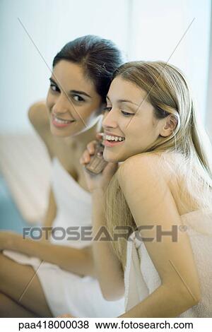 Two young women sitting, wrapped in towels, listening to cell phone together View Large Photo Image Stock Photo - Two young women sitting, wrapped in towels, listening to cell phone together. Fotosearch