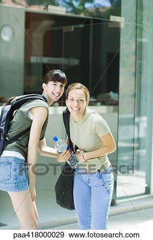 Stock Photo - Two young women standing outdoors in street clothes, smiling at camera. Fotosearch