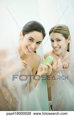 Stock Photo - Two young women taking showers, one handing the other a bar of soap. Fotosearch