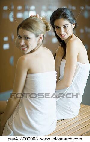 Two young women wrapped in towels, sitting on bench in locker room View Large Photo Image Stock Image - Two young women wrapped in towels, sitting on bench in locker room. Fotosearch