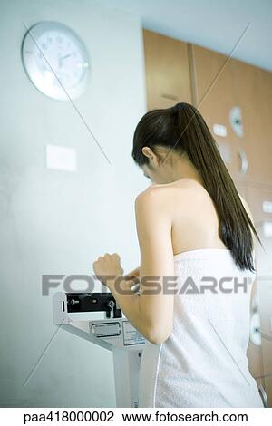 Stock Image - Woman wrapped in towel, standing on scale. Fotosearch