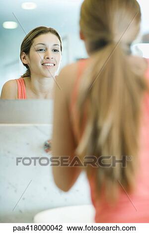 Stock Image - Young woman looking at self in mirror. Fotosearch
