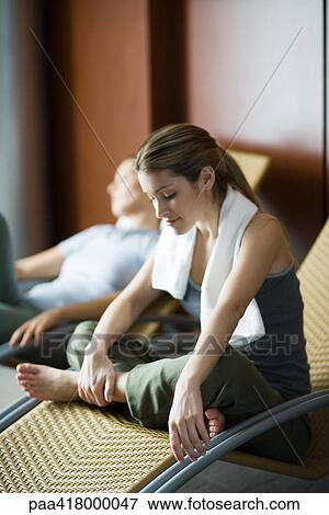 Stock Photo - Young women relaxing in lounge chairs, one sitting indian style, smiling. Fotosearch