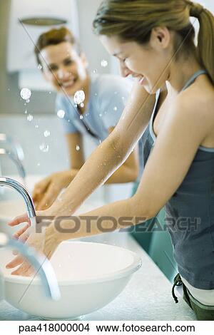 Picture - Young women splashing water in sinks in public restroom. Fotosearch