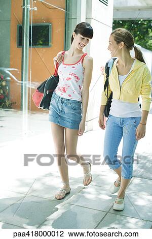 Stock Image - Young women walking on sidewalk in street clothes. Fotosearch