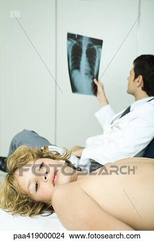 Picture - Boy lying down in doctor's office while doctor looks at x-ray. Fotosearch