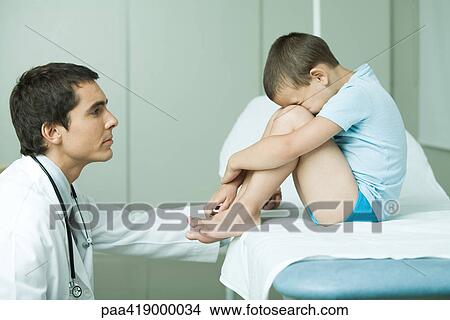 Doctor comforting boy, boy sitting with head down on knees, side view View Large Photo Image Picture - Doctor comforting boy, boy sitting with head down on knees, side view. Fotosearch