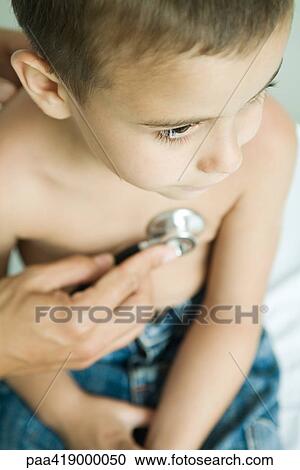 Stock Image - Doctor holding stethoscope to boy's chest. Fotosearch