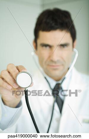 Doctor holding up stethoscope, looking at camera View Large Photo Image Stock Image - Doctor holding up stethoscope, looking at camera. Fotosearch
