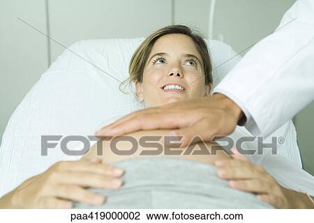 Pregnant woman lying on back in doctor's office, doctor's hand on woman's stomach View Large Photo Image Stock Image - Pregnant woman lying on back in doctor's office, doctor's hand on woman's stomach. Fotosearch