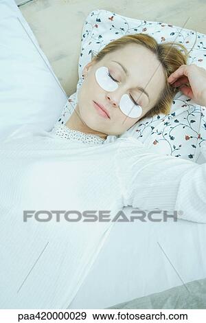 Stock Photo - Woman lying down with eye pads under eyes. Fotosearch