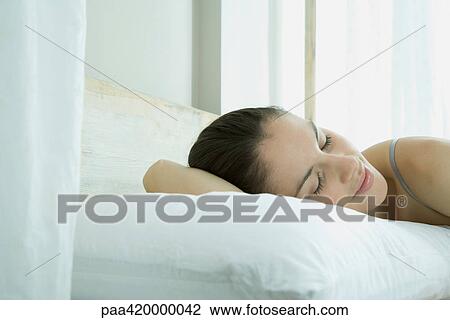 Stock Image - Woman lying in bed, eyes closed and smiling. Fotosearch