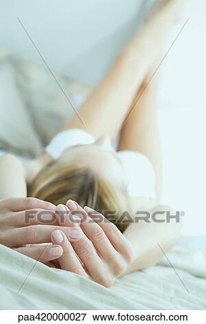 Stock Photo - Woman lying on bed with legs up, focus on hands in foreground. Fotosearch