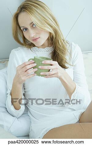 Woman sitting in bed, holding mug, looking at camera View Large Photo Image Stock Photography - Woman sitting in bed, holding mug, looking at camera. Fotosearch