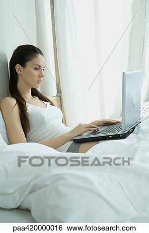 Woman sitting in bed, using laptop View Large Photo Image Stock Photograph - Woman sitting in bed, using laptop. Fotosearch