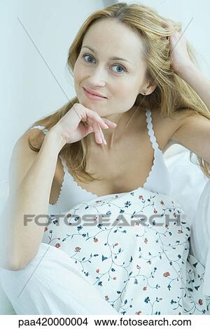 Picture - Woman wearing pajamas, one hand in hair, other hand under chin. Fotosearch