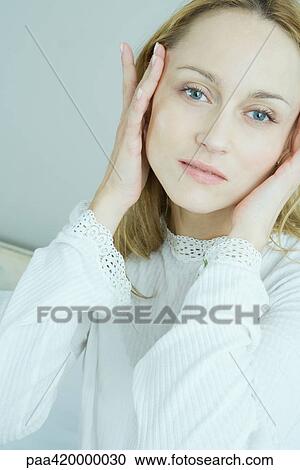 Stock Image - Woman with hands on sides of face, looking at camera. Fotosearch