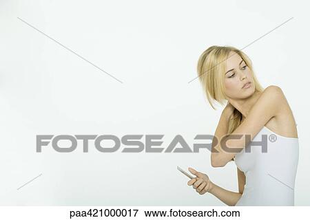 Stock Photo - Teenage girl holding comb, hand in hair, looking over shoulder. Fotosearch