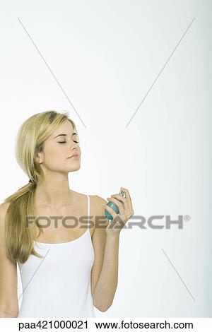 Stock Image - Teenage girl putting on perfume, eyes closed. Fotosearch