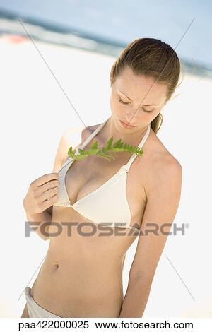 Woman in bikini standing on beach, holding up leaf, waist up View Large Photo Image Stock Photography - Woman in bikini standing on beach, holding up leaf, waist up. Fotosearch