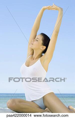 Woman sitting on beach, stretching arms overhead View Large Photo Image Picture - Woman sitting on beach, stretching arms overhead. Fotosearch