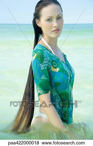 Stock Photo - Woman standing waist deep in sea, looking at camera. Fotosearch
