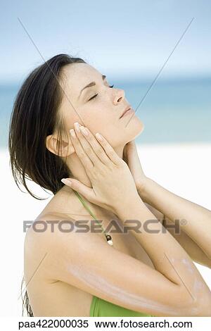 Stock Photography - Woman with sunscreen on arm, hands on either side of face, eyes closed. Fotosearch