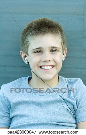Stock Photo - Boy listening to earphones, smiling at camera, portrait. Fotosearch