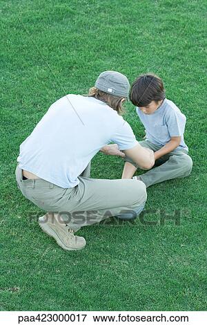 Boy sitting on grass with pants leg rolled up, man leaning over him View Large Photo Image Stock Photo - Boy sitting on grass with pants leg rolled up, man leaning over him. Fotosearch