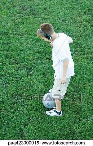 Stock Photography - Boy standing with ball, wearing headphones. Fotosearch