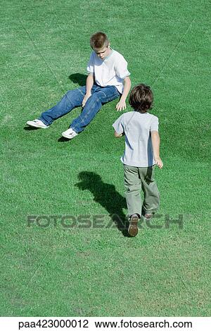 Stock Image - Boy walking across grass toward second boy. Fotosearch