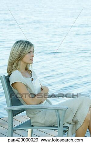 Woman sitting on dock, holding book against chest View Large Photo Image Stock Photo - Woman sitting on dock, holding book against chest. Fotosearch