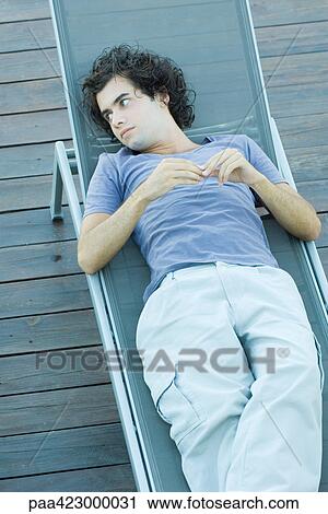 Young man lying on lounge chair View Large Photo Image Stock Image - Young man lying on lounge chair. Fotosearch
