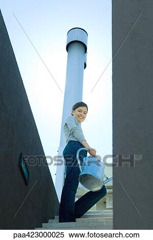 Young woman carrying watering can, low angle view View Large Photo Image Stock Photography - Young woman carrying watering can, low angle view. Fotosearch