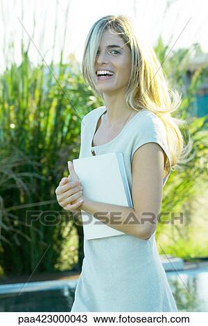 Stock Image - Young woman holding book, laughing. Fotosearch
