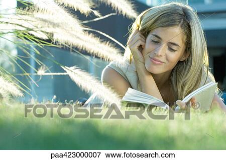 Young woman lying in grass, reading book View Large Photo Image Stock Photo - Young woman lying in grass, reading book. Fotosearch