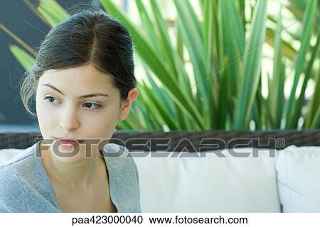 Stock Image - Young woman sitting on outdoor sofa, looking away, portrait. Fotosearch