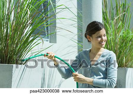 Stock Photo - Young woman watering outdoor plants with hose. Fotosearch
