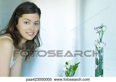 Stock Photography - Young woman with vases of flowers, smiling at camera. Fotosearch