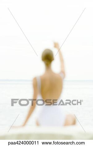 Stock Image - Female figure wearing bathing suit, blurred silhouette, pointing toward sea in background, rear view. Fotosearch